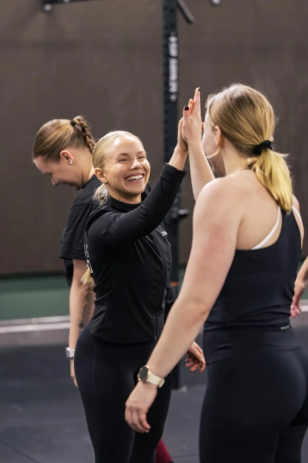 Hymyilevä valmentaja antaa ylävitosen treenaajalle CrossFit-tunnilla.